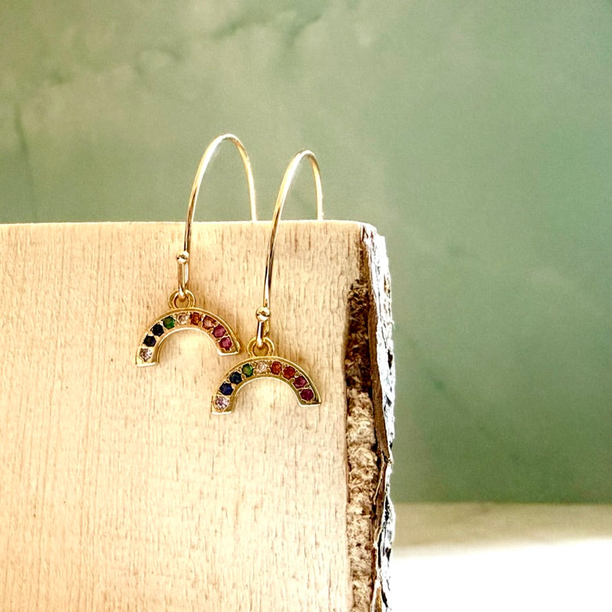 Gold earrings with colorful stones on a wooden block against a green background