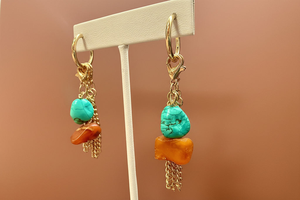 Pair of earrings with turquoise and orange stones on a  stand against a  background