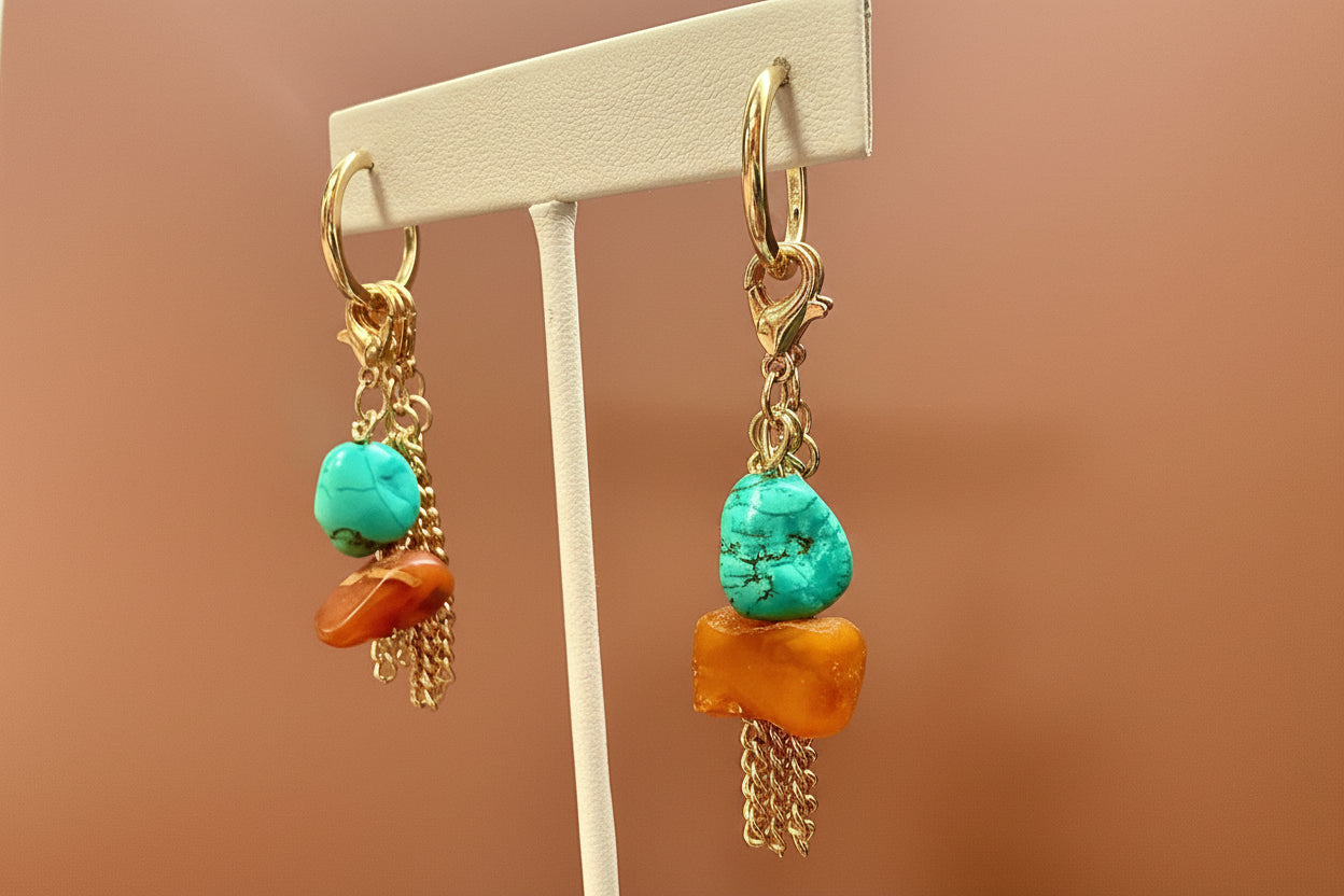 Pair of earrings with turquoise and orange stones on a  stand against a  background